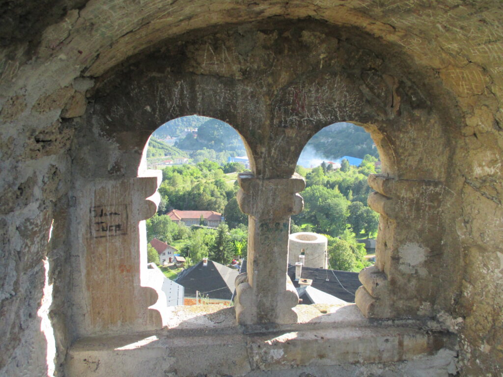Blick durch zwei steinerne Bogenfenster der Festung Jajce auf die Stadt und die umliegenden Berge